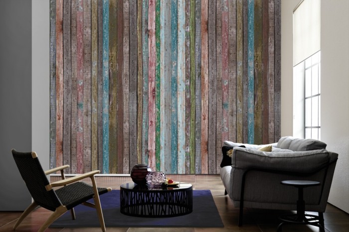 Im Wohnzimmer die Fototapete Holz Wand, bunt gestrichen auf einer großen Wand tapeziert. Die Fototapete Holz Wand, bunt gestrichen ist als Vlies-Fototapete im Wohnzimmer leicht zu tapezieren.