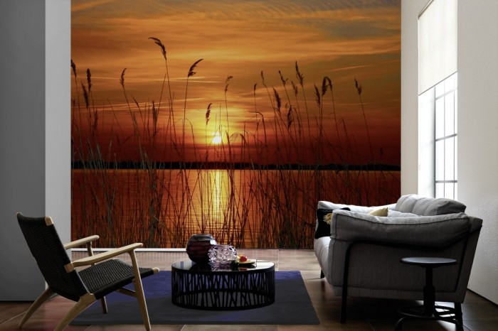 Im Wohnzimmer die Fototapete Seeufer im Sonnenuntergang auf einer großen Wand tapeziert. Die Fototapete Seeufer im Sonnenuntergang ist als Vlies-Fototapete im Wohnzimmer leicht zu tapezieren.