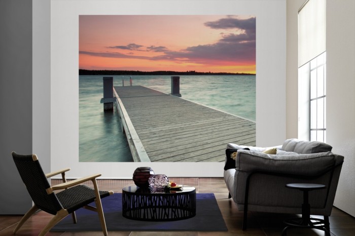 Die Fototapete Steg im See bei Sonnenaufgang als große Bildtapete im Wohnzimmer. Als Bildtapete ist die Fototapete Steg im See bei Sonnenaufgang ein besonderes Highlight auf Vliestapete.