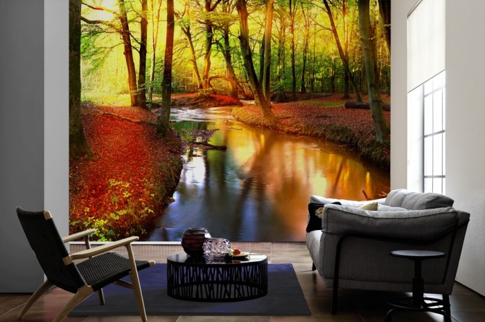 Im Wohnzimmer die Fototapete Waldbach im Sonnenlicht auf einer großen Wand tapeziert. Die Fototapete Waldbach im Sonnenlicht ist als Vlies-Fototapete im Wohnzimmer leicht zu tapezieren.