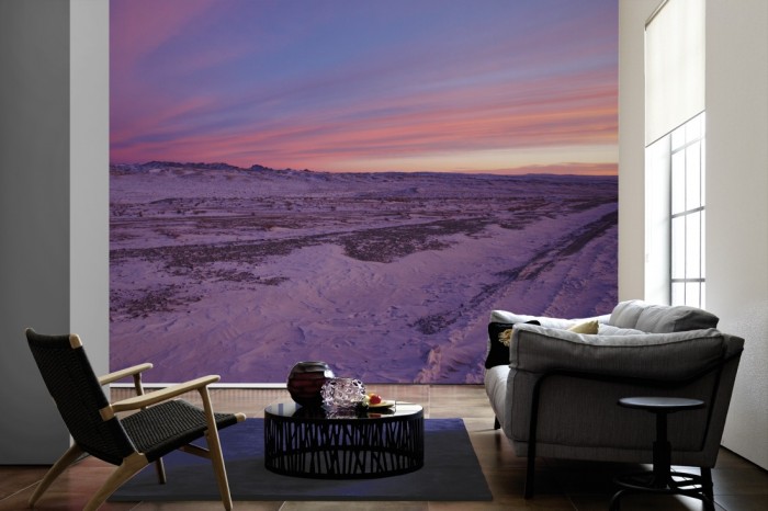 Im Wohnzimmer die Fototapete Schneelandschaft bei Sonnenuntergang auf einer großen Wand tapeziert. Die Fototapete Schneelandschaft bei Sonnenuntergang ist als Vlies-Fototapete im Wohnzimmer leicht zu tapezieren.