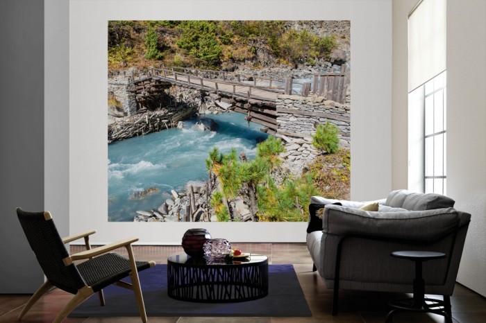 Die Fototapete Bach mit Holzbrücke im Gebirge als große Bildtapete im Wohnzimmer. Als Bildtapete ist die Fototapete Bach mit Holzbrücke im Gebirge ein besonderes Highlight auf Vliestapete.