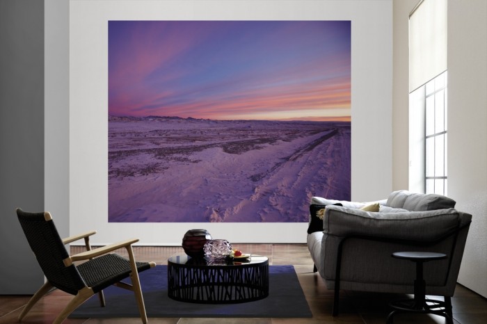 Die Fototapete Schneelandschaft bei Sonnenuntergang als große Bildtapete im Wohnzimmer. Als Bildtapete ist die Fototapete Schneelandschaft bei Sonnenuntergang ein besonderes Highlight auf Vliestapete.