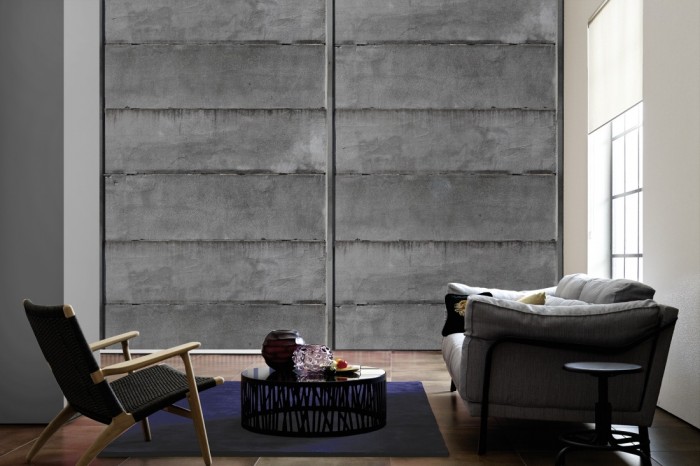 Im Wohnzimmer die Fototapete Beton Wand, Betonplatten auf einer großen Wand tapeziert. Die Fototapete Beton Wand, Betonplatten ist als Vlies-Fototapete im Wohnzimmer leicht zu tapezieren.