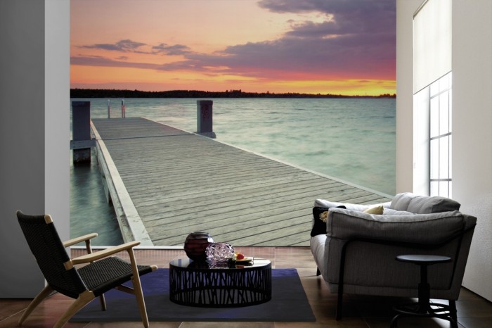 Im Wohnzimmer die Fototapete Steg im See bei Sonnenaufgang auf einer großen Wand tapeziert. Die Fototapete Steg im See bei Sonnenaufgang ist als Vlies-Fototapete im Wohnzimmer leicht zu tapezieren.