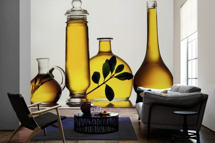 Im Wohnzimmer die Fototapete Olivenöl in Glasflaschen auf einer großen Wand tapeziert. Die Fototapete Olivenöl in Glasflaschen ist als Vlies-Fototapete im Wohnzimmer leicht zu tapezieren.