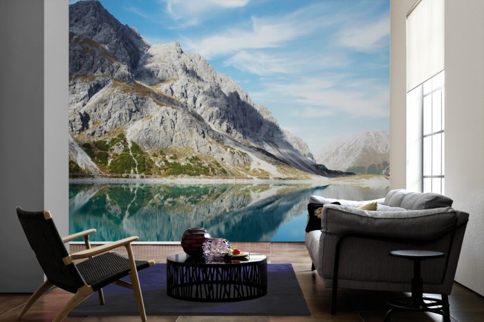Im Wohnzimmer die Fototapete Stiller Bergsee in den Alpen auf einer großen Wand tapeziert. Die Fototapete Stiller Bergsee in den Alpen ist als Vlies-Fototapete im Wohnzimmer leicht zu tapezieren.