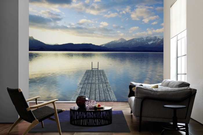 Im Wohnzimmer die Fototapete Steg im See in den Alpen auf einer großen Wand tapeziert. Die Fototapete Steg im See in den Alpen ist als Vlies-Fototapete im Wohnzimmer leicht zu tapezieren.