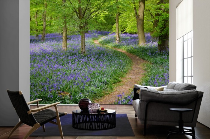 Im Wohnzimmer die Fototapete Waldweg mit Blumen im Sommer auf einer großen Wand tapeziert. Die Fototapete Waldweg mit Blumen im Sommer ist als Vlies-Fototapete im Wohnzimmer leicht zu tapezieren.