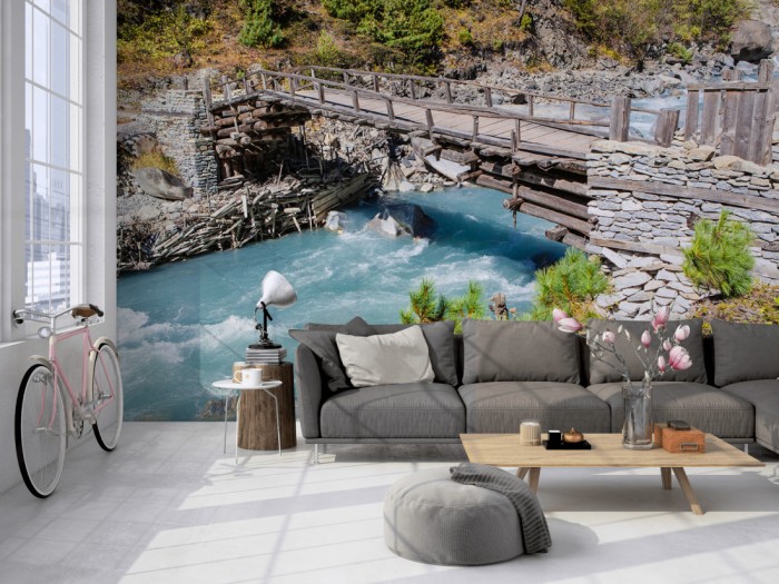 Die Fototapete Bach mit Holzbrücke im Gebirge auf einer großen Wand im Loft tapeziert. Die Fototapete Bach mit Holzbrücke im Gebirge wird individuell auf Deine Wand angepasst.