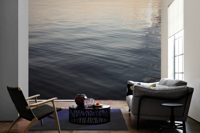 Im Wohnzimmer die Fototapete Stiller See in der Abendsonne auf einer großen Wand tapeziert. Die Fototapete Stiller See in der Abendsonne ist als Vlies-Fototapete im Wohnzimmer leicht zu tapezieren.