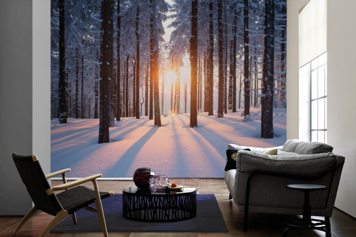 Im Wohnzimmer die Fototapete Wald im Schnee bei Sonnenaufgang auf einer großen Wand tapeziert. Die Fototapete Wald im Schnee bei Sonnenaufgang ist als Vlies-Fototapete im Wohnzimmer leicht zu tapezieren.